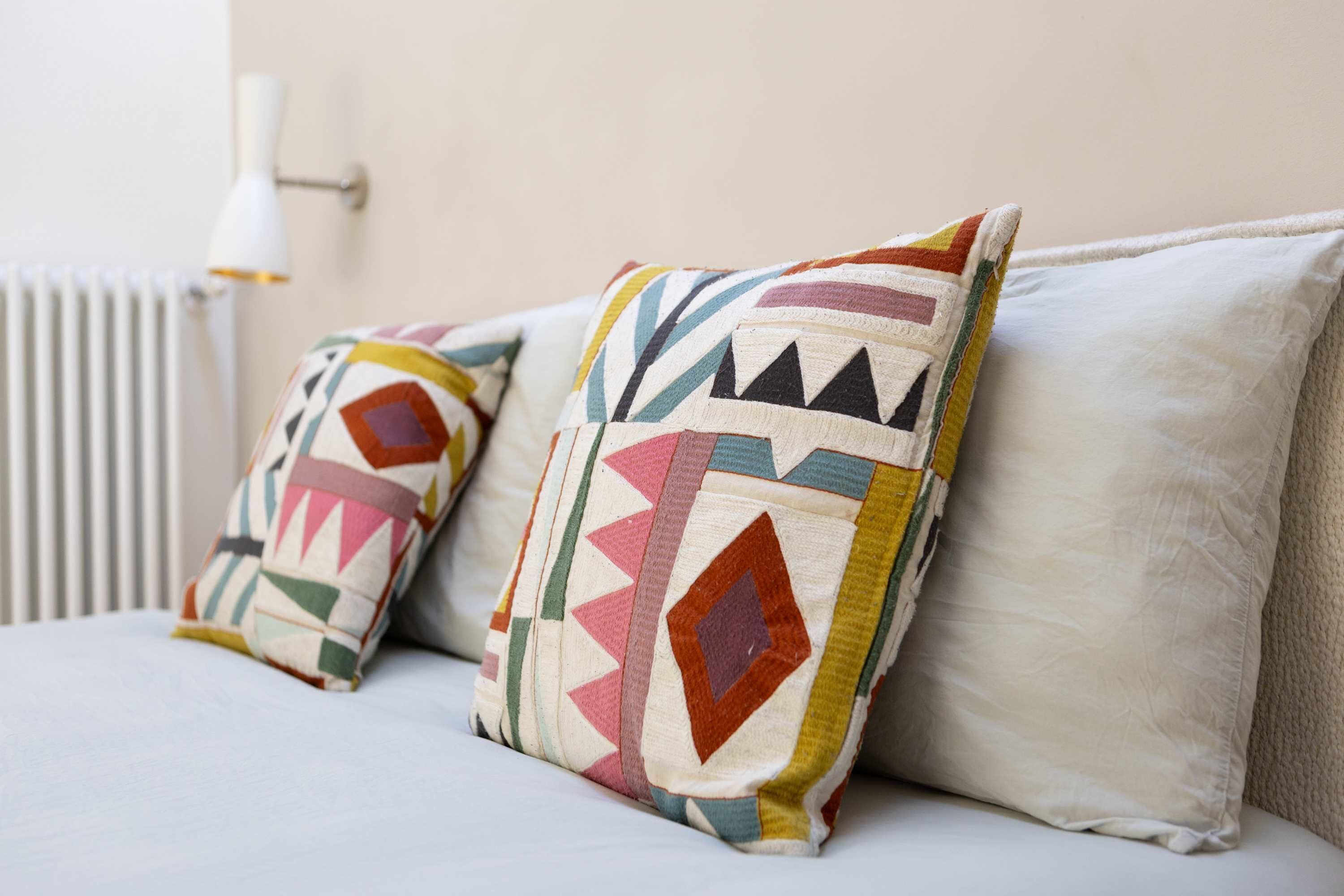 Cama com duas almofadas e parede branca.