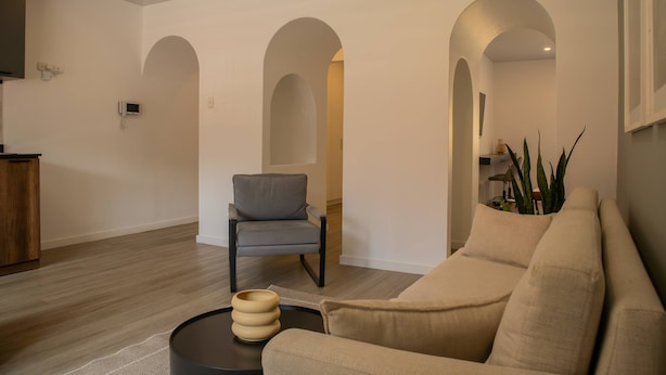Un salon comprenant un canapé, un fauteuil, une table basse et une plante. Trois arches donnent accès à d’autres pièces.
