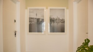 Un couloir avec deux photographies en noir et blanc représentant des paysages urbains, encadrées et accrochées au mur, un plancher en bois et une porte sur la gauche.