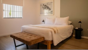 Une chambre à coucher avec un lit, un banc, une table de chevet, une lampe et un tableau encadré au mur.