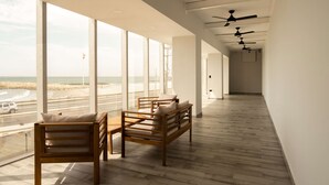 A modern hotel room with large windows, a wooden floor, and ceiling fans.