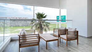 A balcony with a view of a fort and palm tree, furnished with wooden chairs and a table.