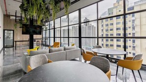 Um espaço de escritório moderno com uma janela ampla, um sofá, uma mesa redonda e plantas penduradas.