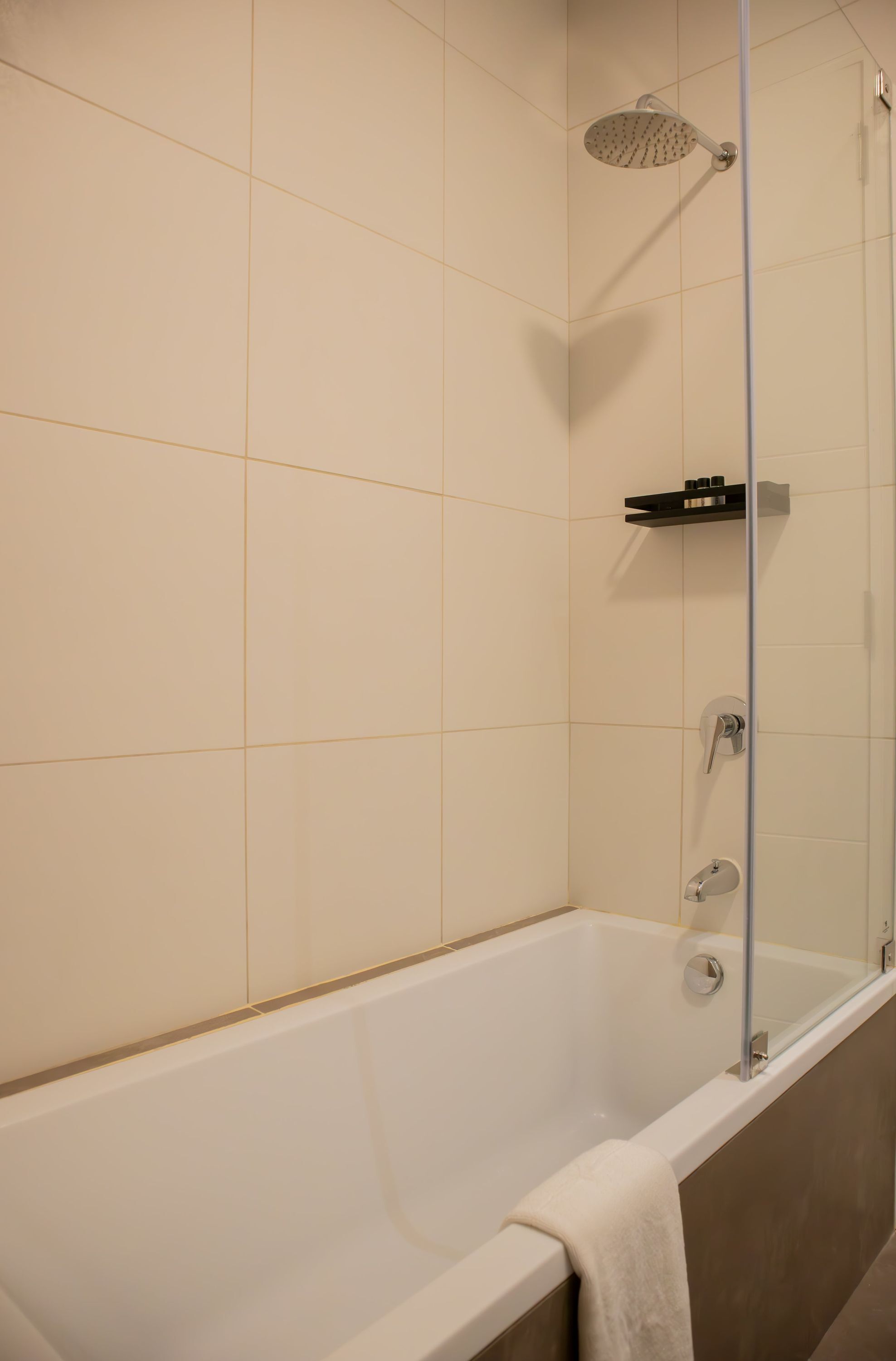 A modern bathroom with a bathtub, a showerhead, and a shelf with toiletries.