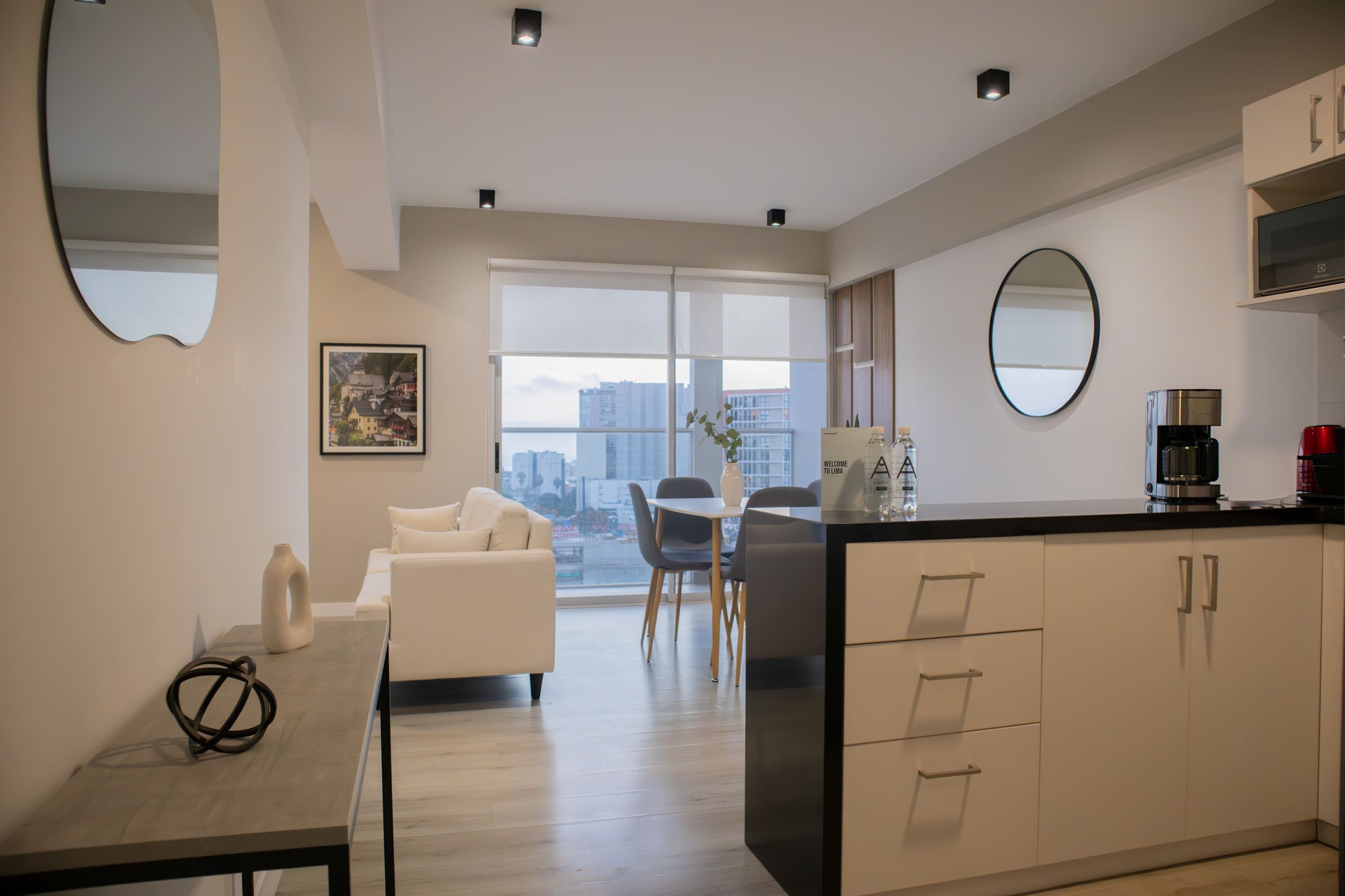 A modern kitchen with a dining area, a sofa, and a large window with a city view.