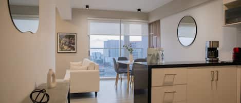 A modern kitchen with a dining area, a sofa, and a large window with a city view.