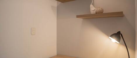A corner desk with a black chair, a desk lamp, and two wooden shelves with decorative items.