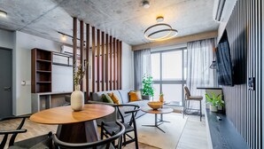 A modern living room with a round wooden dining table, black chairs, a sofa with cushions, a side table with a bowl and plant, and a large window with curtains. - w Stunning 2BR w Great Deco in Centriqo (Veracruz)