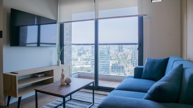 Una sala de estar moderna con un ventanal grande, un televisor de pantalla plana, un sofá azul y una mesa de centro de madera.