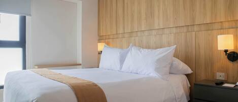 Une chambre d’hôtel avec un grand lit, une tête de lit en bois, deux lampes de chevet et une table de chevet.