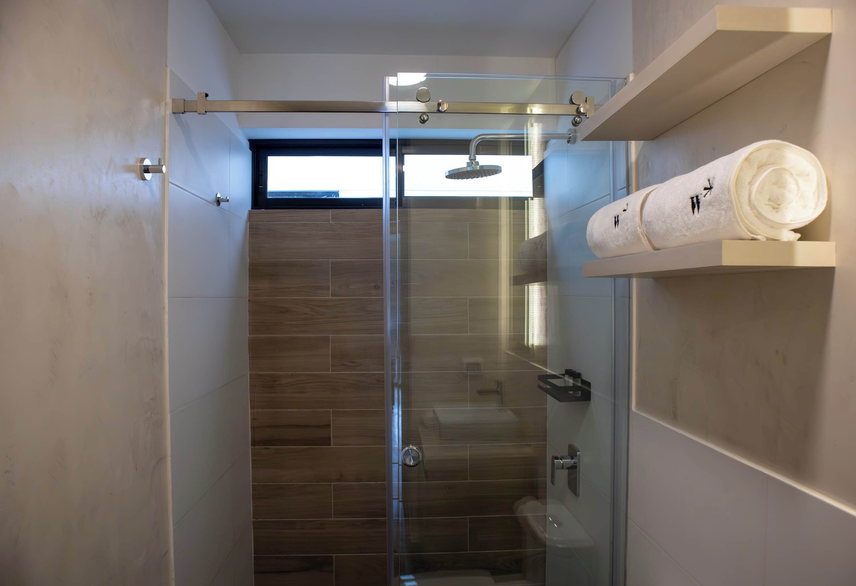 A modern bathroom with a glass-enclosed shower, wooden flooring, and a towel rack with towels.