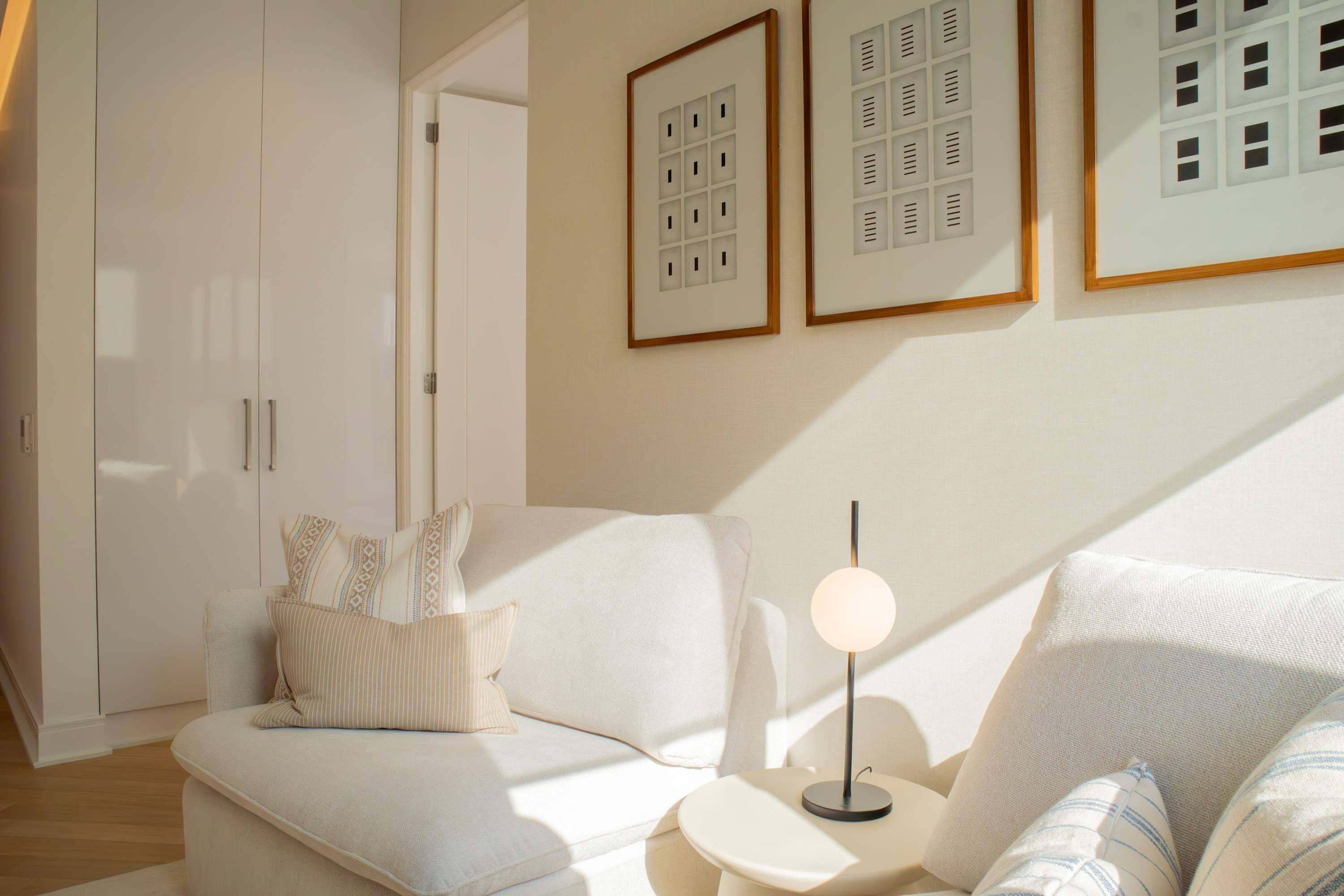 Una sala moderna con un sofá, una mesita auxiliar y una lámpara. Hay cuadros enmarcados en la pared y una puerta que da a otra habitación.