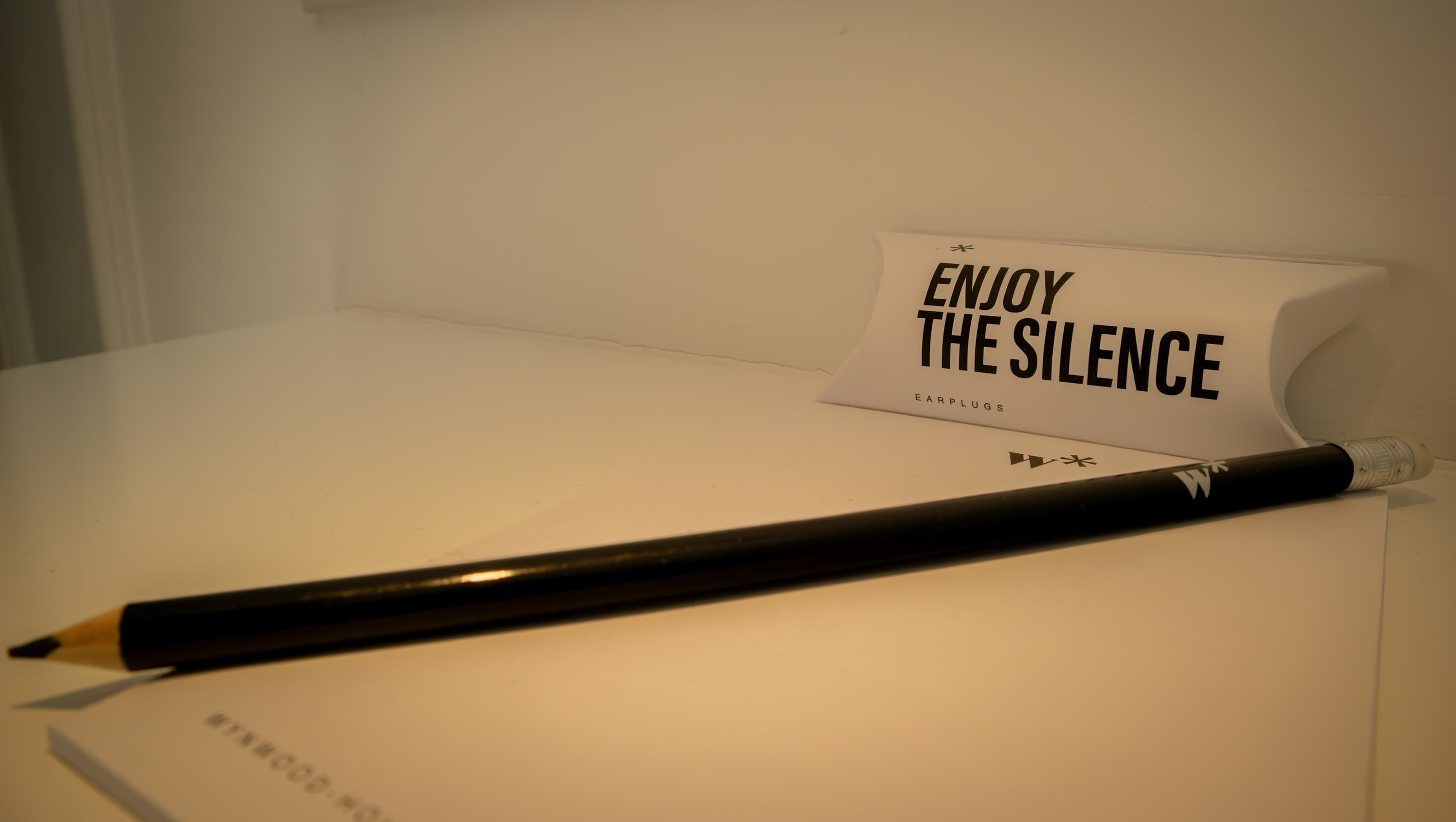 Une table blanche avec un crayon noir et une pancarte sur laquelle on peut lire « PROFITEZ DU SILENCE », avec le nom de la marque « BOULES QUIETS » en dessous.