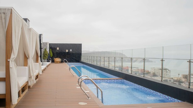 Une piscine sur le toit offrant une vue sur la ville, une terrasse en bois et des chaises longues.