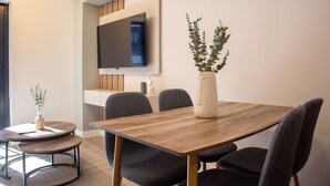 A modern dining area with a wooden table, four chairs, a vase with plants, and a flat-screen TV mounted on the wall. - w Stunning 1BR in Miraflores (Lima)