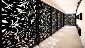 A hallway with patterned black metal screens, a concrete floor, and a white wall.