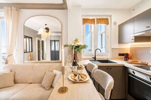 A modern kitchen with a central island, a dining area with a sofa, and a view of the city through large windows.