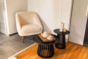 A room with a plush armchair, a small round table with a teapot and cup, and a matching side table with books.