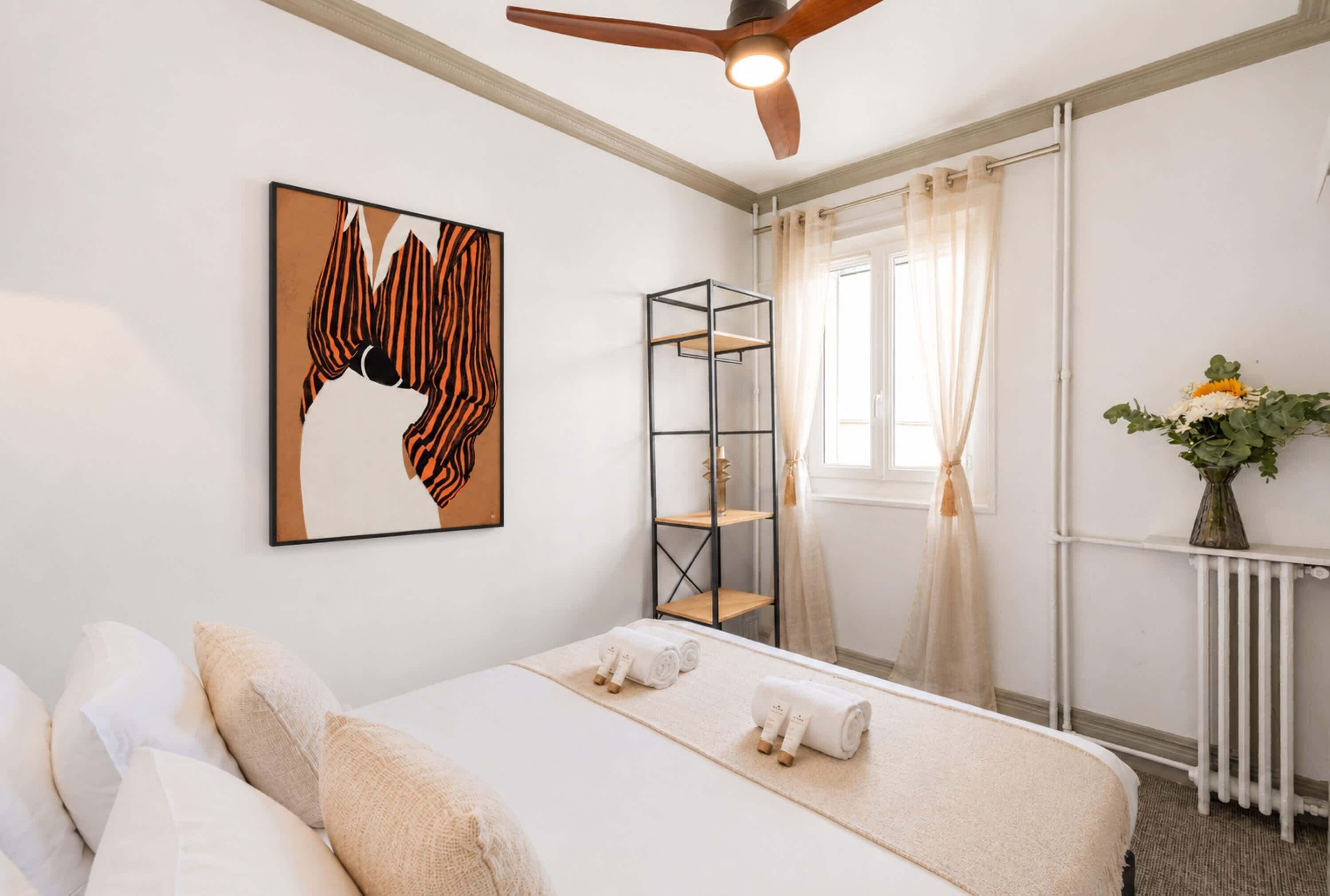Ein Hotelzimmer mit einem Bett, einem Deckenventilator, einem fenster mit Vorhängen, einer Heizung und einem an der Wand montierten Regal.