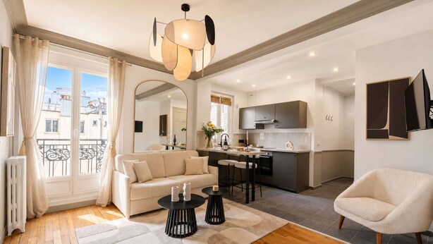 A modern apartment with a living room, kitchen, and dining area. There is a sofa, a coffee table, and a chair. The kitchen has a sink and a stove. The apartment has a balcony with a view of the city. - Elegant apartment with lift - Gare de Lyon & Bercy (Paris)