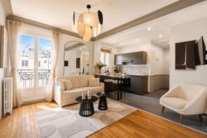 A modern apartment with a living room, kitchen, and dining area. There is a sofa, a coffee table, and a chair. The kitchen has a sink and a stove. The apartment has a balcony with a view of the city.
