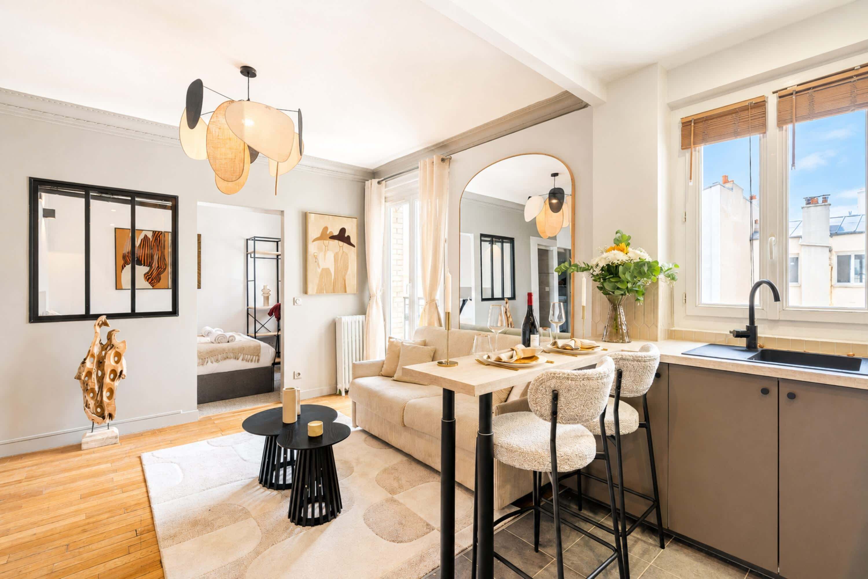 Ein modernes Wohnzimmer mit einer Couch, einem Esstisch und Stühlen, einer Küchenzeile mit Spüle und Fenster sowie Kunstwerken an den Wänden.
