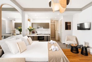 A modern hotel room with a large bed, a sitting area with a chair, a small table, a flat-screen TV mounted on the wall, and a kitchenette in the background. - Elegant apartment with lift - Gare de Lyon & Bercy (Paris)