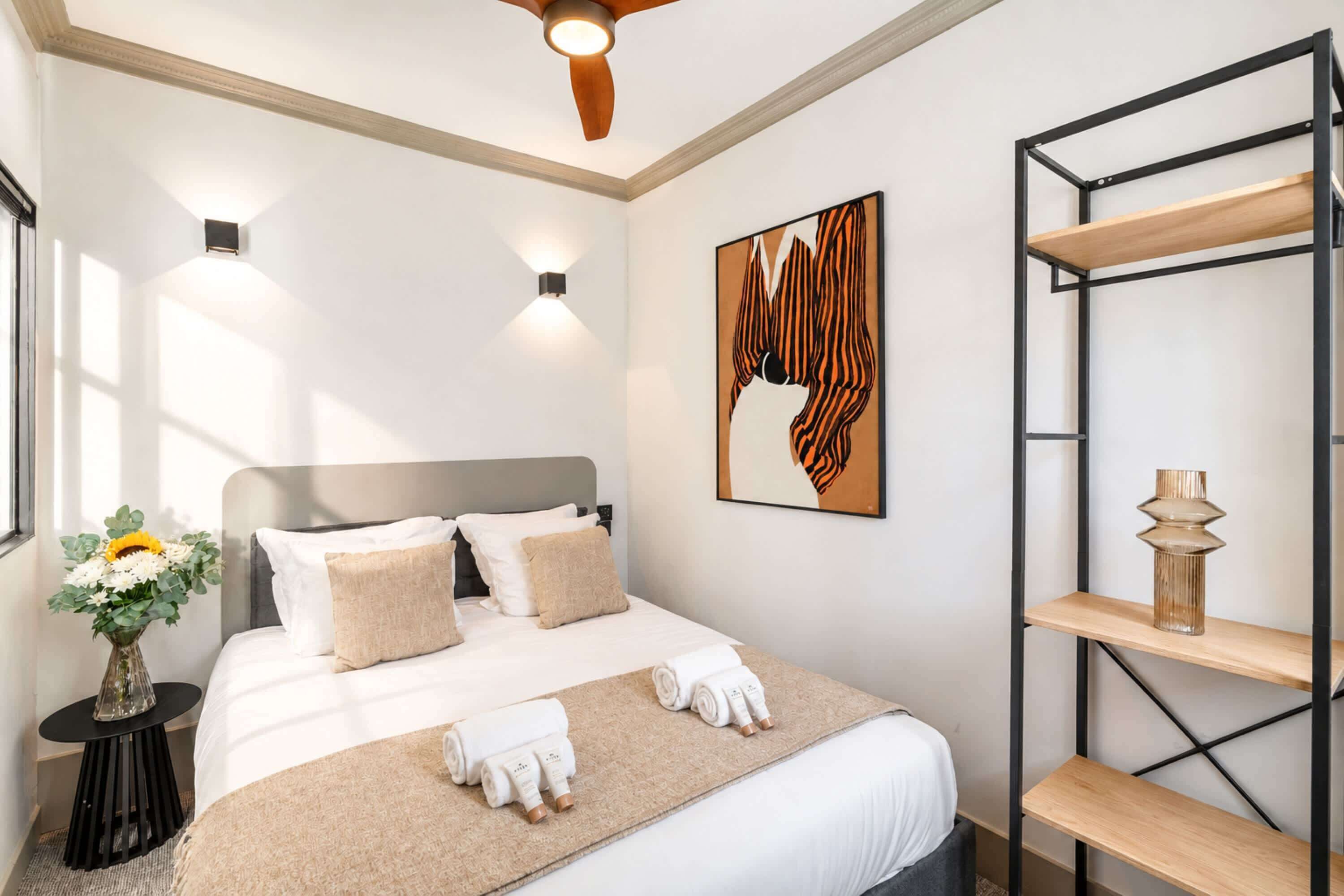 Ein Hotelzimmer mit Bett, Nachttisch, Wandregal und Deckenventilator.