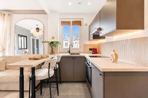 A compact kitchen with a dining area, a built-in oven, and a window with blinds.