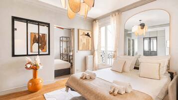 Une chambre à coucher moderne avec un grand lit, un miroir, des œuvres d’art au mur et une vue sur l’extérieur.