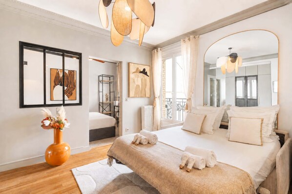 A modern bedroom with a large bed, a mirror, artwork on the wall, and a view of the outside.