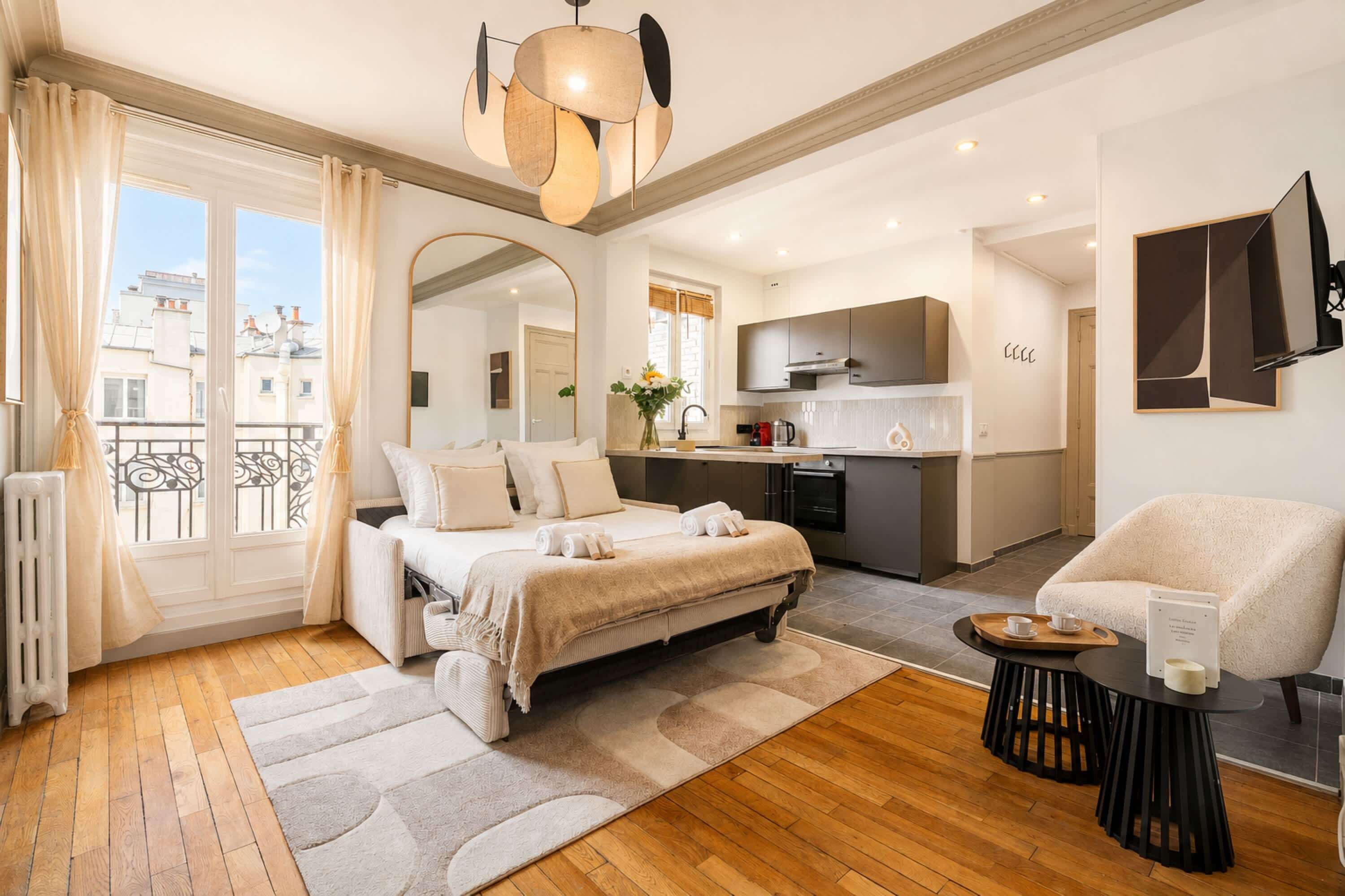Ein modernes Hotelzimmer mit Bett, Sitzecke, einer Küche und einem Balkon mit Vorhängen.