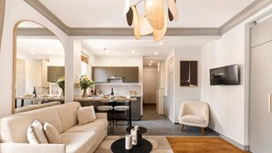 A modern living room with a sofa, a coffee table, and a TV. There is a kitchen in the background with a dining area. - Elegant apartment with lift - Gare de Lyon & Bercy (Paris)