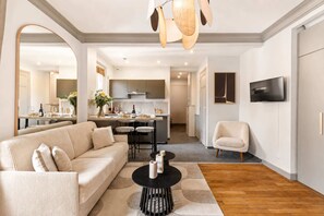 A modern living room with a sofa, a coffee table, and a TV. There is a kitchen in the background with a dining area. - Elegant apartment with lift - Gare de Lyon & Bercy (Paris)