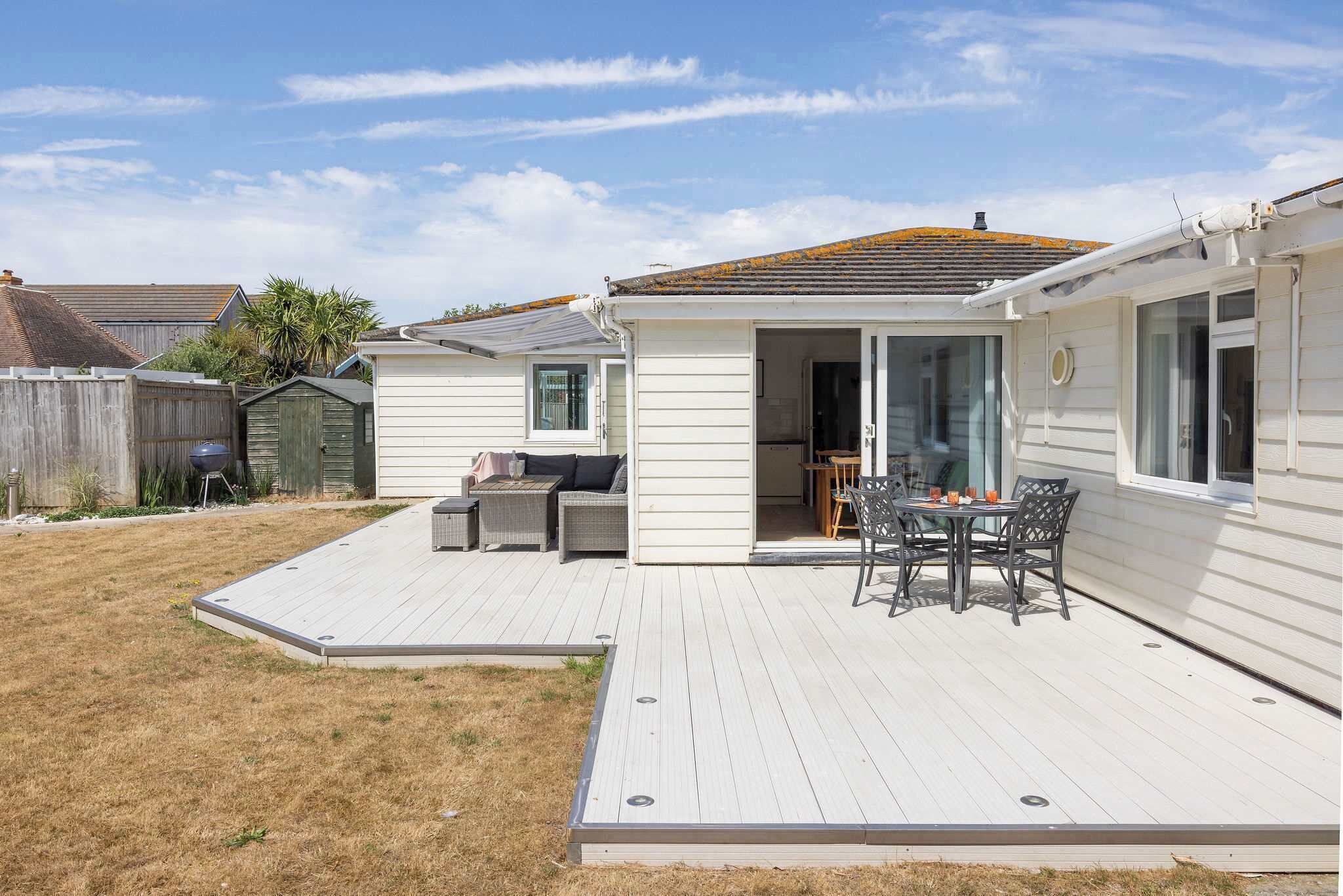 A single-story mobile home with a covered patio area, a small outdoor seating area, and a fenced backyard.