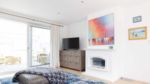 Een moderne woonkamer met een groot raam, een open haard, een televisie en een schilderij aan de muur.