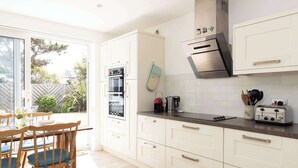 Een moderne keuken met witte kasten, een roestvrijstalen afzuigkap, en een eetgedeelte met houten stoelen en een tafel.