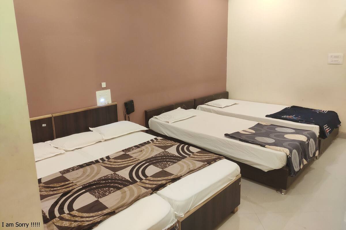 A hotel room with three single beds, each with a patterned bedspread. There is a small table with a lamp and a phone on the wall.
