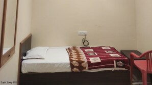 A small, single-bed room with a ceiling fan, recessed lighting, and a red chair. - Krishan Bhavan And Events (Nagaur)