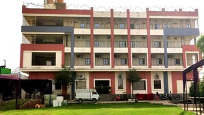 A multi-story building with a central entrance, surrounded by a grassy area and a parked truck. - Krishan Bhavan And Events (Nagaur)