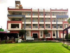 Un edificio de varios pisos con una entrada central, rodeado de césped y una camioneta estacionada.