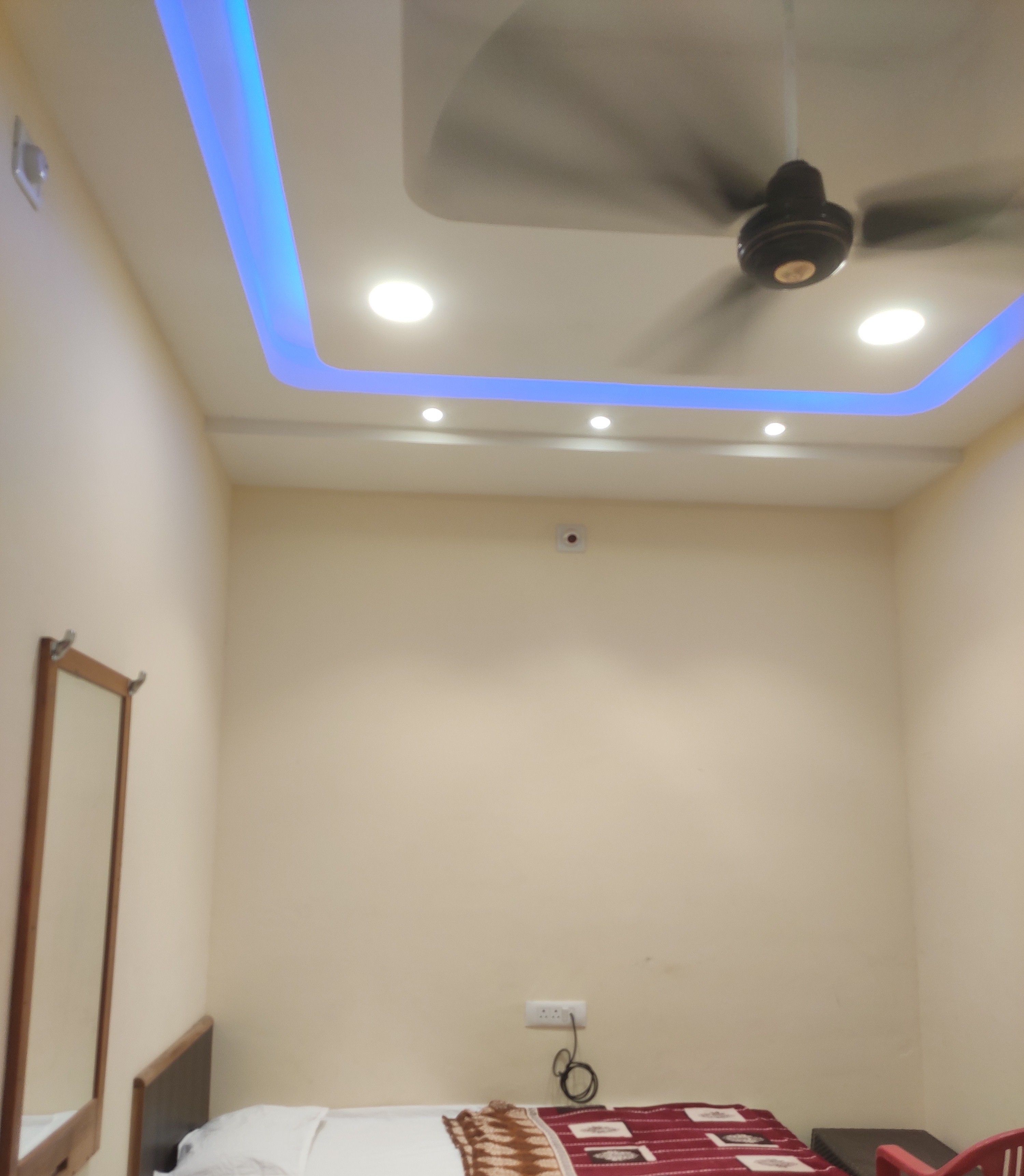 A small, single-bed room with a ceiling fan, recessed lighting, and a red chair.