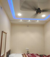 Una habitación pequeña con cama individual, ventilador de techo, iluminación empotrada y una silla roja.