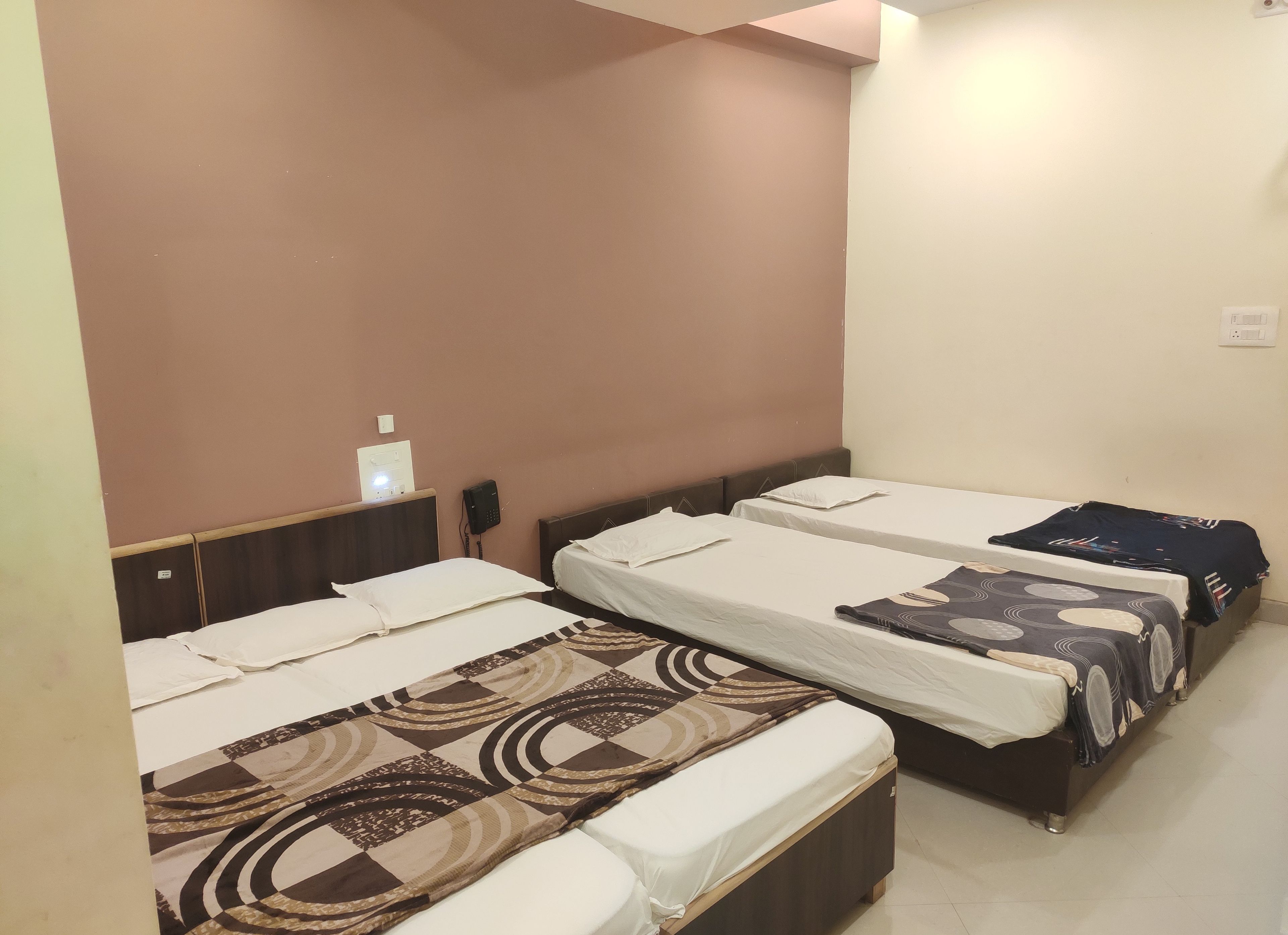 Habitación de hotel con tres camas individuales, cada una con una colcha estampada. Hay una mesita con una lámpara y un teléfono en la pared.