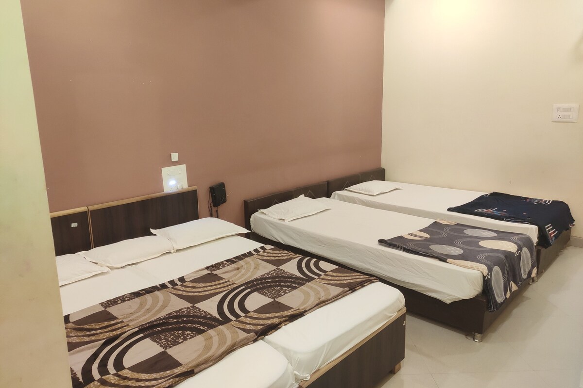 A hotel room with three single beds, each with a patterned bedspread. There is a small table with a lamp and a phone on the wall.