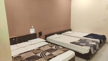 Habitación de hotel con tres camas individuales, cada una con una colcha estampada. Hay una mesita con una lámpara y un teléfono en la pared.