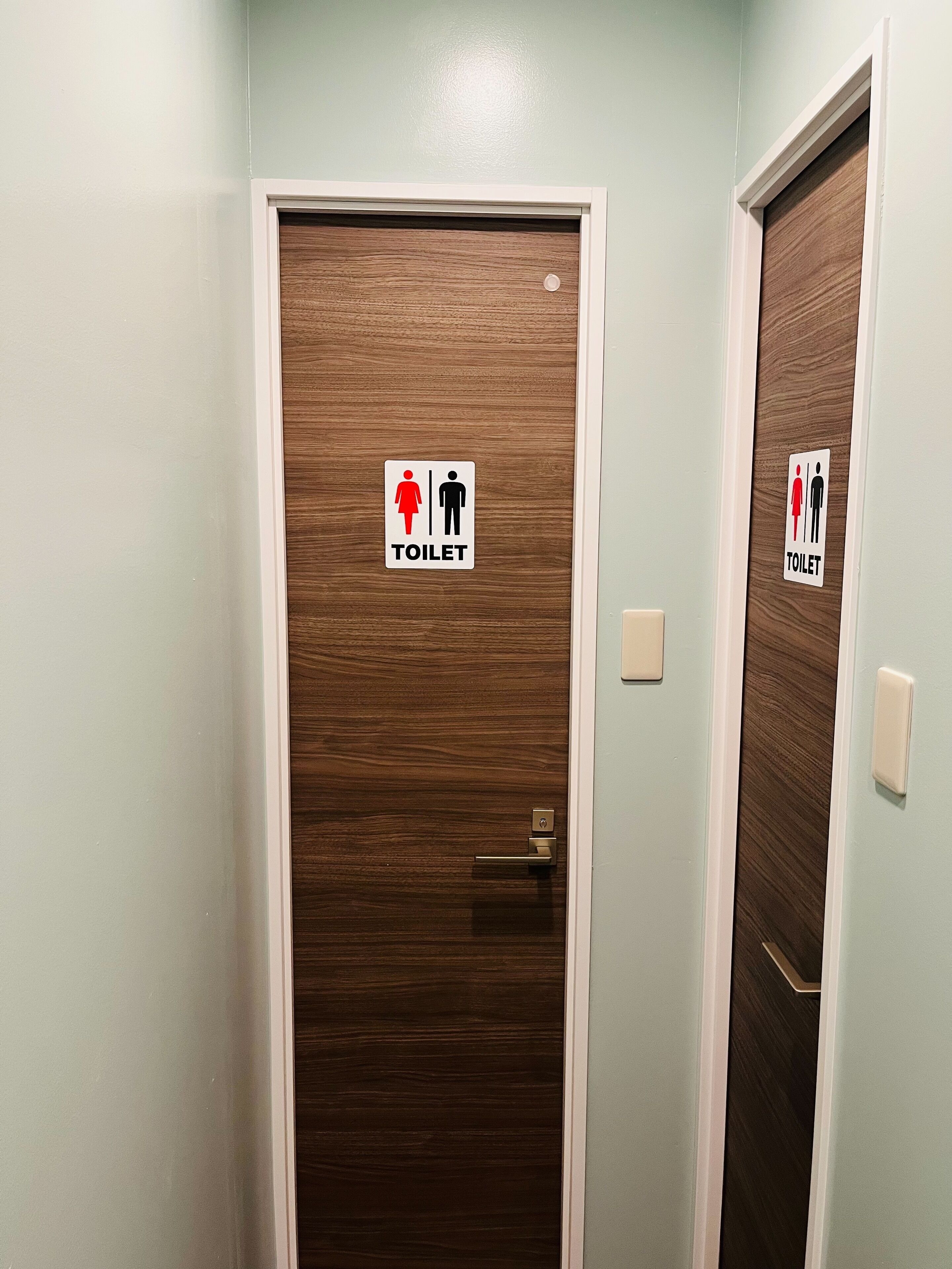 Une porte avec un panneau en bois et un cadre blanc, portant un symbole indiquant la présence de toilettes.