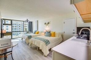 Una habitación de hotel moderna con dos camas, una zona de cocina y un ventanal con vistas a la ciudad.