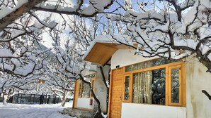 A small wooden building with a large window, surrounded by snow-covered trees. - Nine Apple Resort Dharali Harsil (Bhatwari)