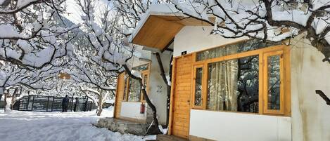 A small wooden building with a large window, surrounded by snow-covered trees.